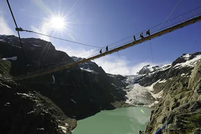 Alpencamping - Brücke mit Wanderern darauf in den Alpen über einem Bergsee