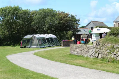 Beacon Cottage Farm Holidays - Zelt auf der Zeltwiese unter schattenspendenden Bäumen und ein Wohnmobil vor den Gebäuden des Campingplatzes