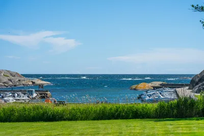 Blick auf das Meer mit Strandliegen und Felsen am Ufer, davor grünes Gras und ein Campingplatzbereich.