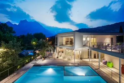 Camping Al Porto - Das Hauptgebäude des Campingplatz mit Swimmingpools und Sitzgelegenheiten, sowie einem Balkon mit Sonnenliegen bei Nacht