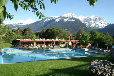 Camping Bella-Tola - Swimmingpoo mit Sonnenliegen und Liegewiese mit den Alpen im Hintergrund