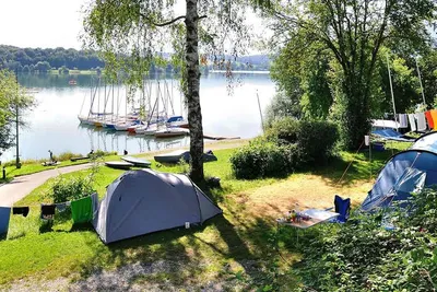 Camping Brugger am Riegsee  -  Zeltplatz vom Campingplatz zwischen Bäumen mit Blick auf die Anlegestelle und den See