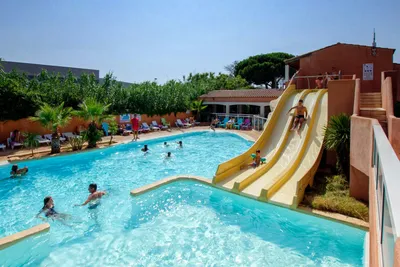 Großer Camping-Pool mit Wasserrutsche, Liegen am Beckenrand und mehreren Personen im Wasser.