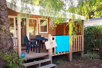 Holzterrasse am Campingplatz mit Sitzgruppe, Tisch und Stühlen, daneben Wäscheleine und Hecke im Gartenbereich.