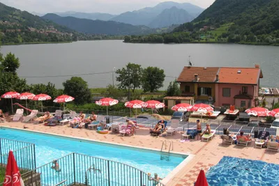 Camping La Tartufaia - Poolanlage mit Liegestühlen und Sonnenschirmen und der Lago di Endine im Hintergrund