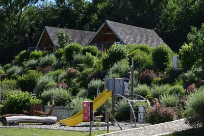 Camping Les 12 Cols - Kinderspielplatz auf mit Rutsche und Kletternetz mit Hütten auf einem Hügel im Hintergrund