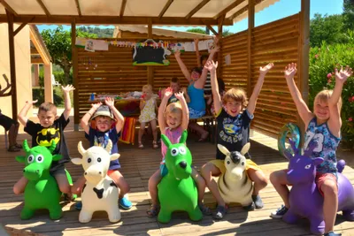 Kinder auf der Holzterrasse vor einer überdachten Bühne mit Deko, Spielzeugfiguren und bunten Girlanden im Campingbereich.