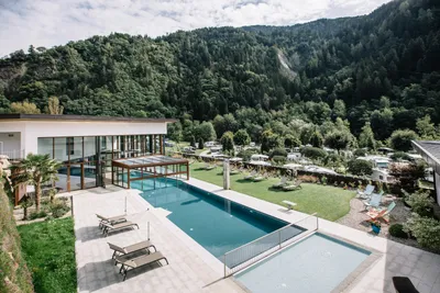 Schwimmbecken am Campingplatz mit Liegen auf der Terrasse, Blick auf Wald und Berge im Hintergrund.