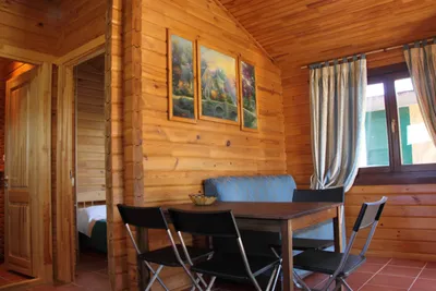 Camping Puerta de la Demanda - Hauptzimmer eines Holzbungalows mit Tisch und Stühlen