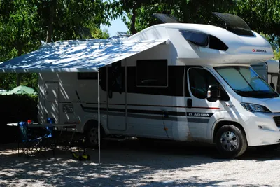 Camping Ribamar - Wohnmobil mit Vordach auf einem mit Kies ausgelegten Standplatz im Halbschatten unter Bäumen