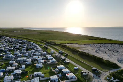 Campingplatz an der Küste mit Wohnwagen und Stellplätzen, Weg zum Strand und Blick aufs Meer.
