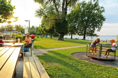Campingplatz Strandbad, Amriswil - Camper sitzen auf der Terrrasse des Campingplatzes neben dem Kinderspielplatz