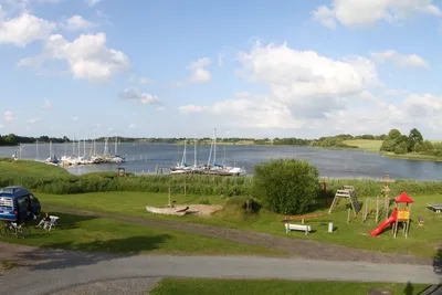 Campingplatz Wees - Kinderspielplatz auf dem Campingplatz mit Rutsche, Klettergerüst und Wippe mit Wasser des Ostseefjords im Hintergrund
