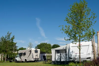 Wohnmobile und Vorzelt auf einem Campingplatz, mit Stühlen am Stellplatz und Bäumen im Hintergrund.