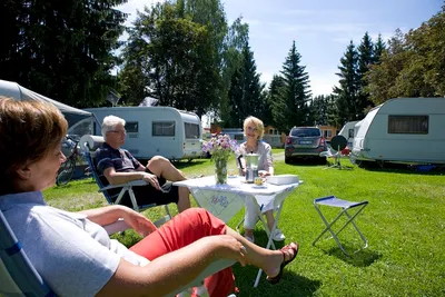 Kur- und Vitalcamping - Gäste vor den Wohnwagen auf der Wiese des Campingplatzes umrandet von Bäumen