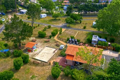 Luftaufnahme eines Campingplatzes mit Wohnwagen, Wegen und mehreren Stellplätzen zwischen Bäumen und gepflegten Grünflächen.