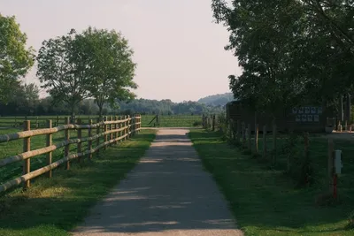 Campingweg mit Holzzaun, Rasen und Bäumen, im Hintergrund Hügel und ein Gebäude mit Fenstern.