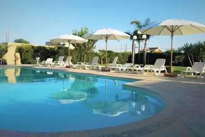 Schwimmbad mit Liegestühlen und Sonnenschirmen am Campingplatz, im Hintergrund Hecken und Bäume.