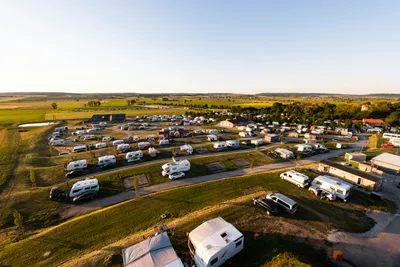 Luftaufnahme eines Campingplatzes mit vielen Wohnmobilen und Wohnwagen, Straßen und Stellplätzen in grüner Landschaft.