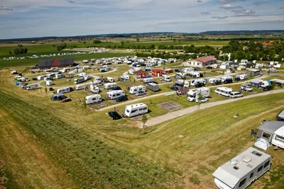 Luftaufnahme eines Campingplatzes mit vielen Wohnmobilen und Wohnwagen auf Wiesen, Feldwegen und einzelnen Stellplätzen.