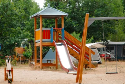 Spielplatz-Rutsche an einem hölzernen Kletterturm, im Hintergrund Zelte und Bäume auf dem Campingplatz.