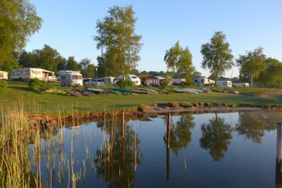 Naturcamping Hellör - Stellplätze im Schatten unter Bäumen mit Kanus am See auf dem Campingplatz