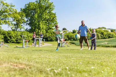 Ostsee-Campingplatz Kagelbusch  - Fußball spielende Camper auf grüner Wiese vom Campingplatz, Outdoor Fitness Bereich im Hintergrund