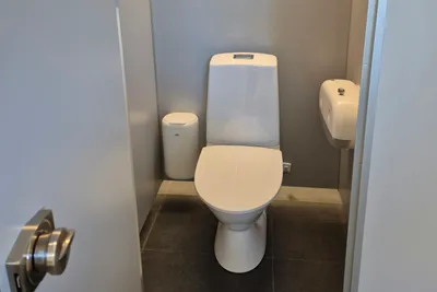 Weiße Toilette im modernen Badezimmer mit Fliesenboden und geschlossener Tür, seitlich ein kleines Waschbecken.