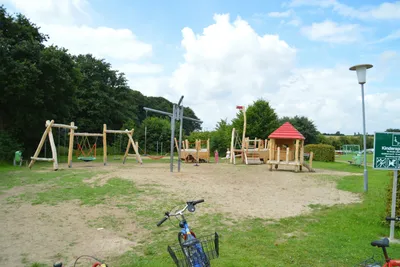 Campingpark Schlei-Karschau - Kinderspielplatz mit Schaukeln neben Bäumen auf dem Campingplatz