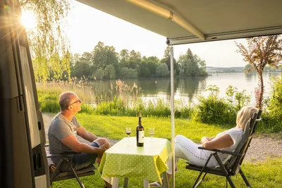 Camping Schwanenplatz - Camper sitzen gemeinsam auf ihrem Standplatz mit Blick auf den See
